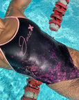 Female Model wearing the Flower of life One-Piece Swimsuit in black while lying in the water at the pool.