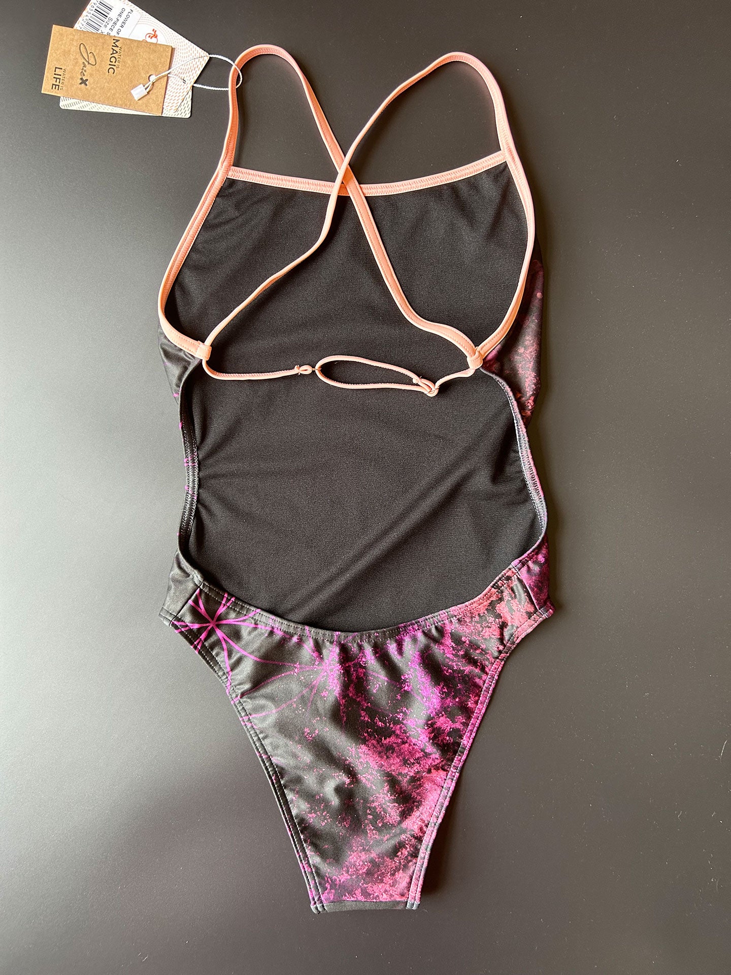 Flower of life One-Piece Swimsuit in black lying on a black surface shown from the back for more details to the open back and adjustable straps.