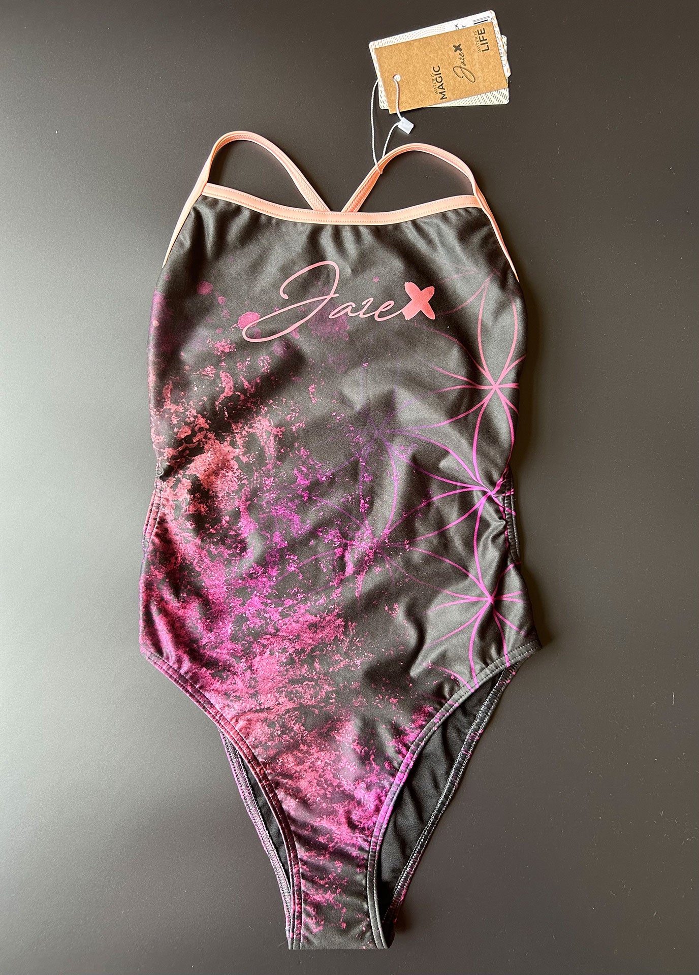 Flower of life One-Piece Swimsuit in black lying on a black surface shown from the front with focus on the hand drawn pattern.