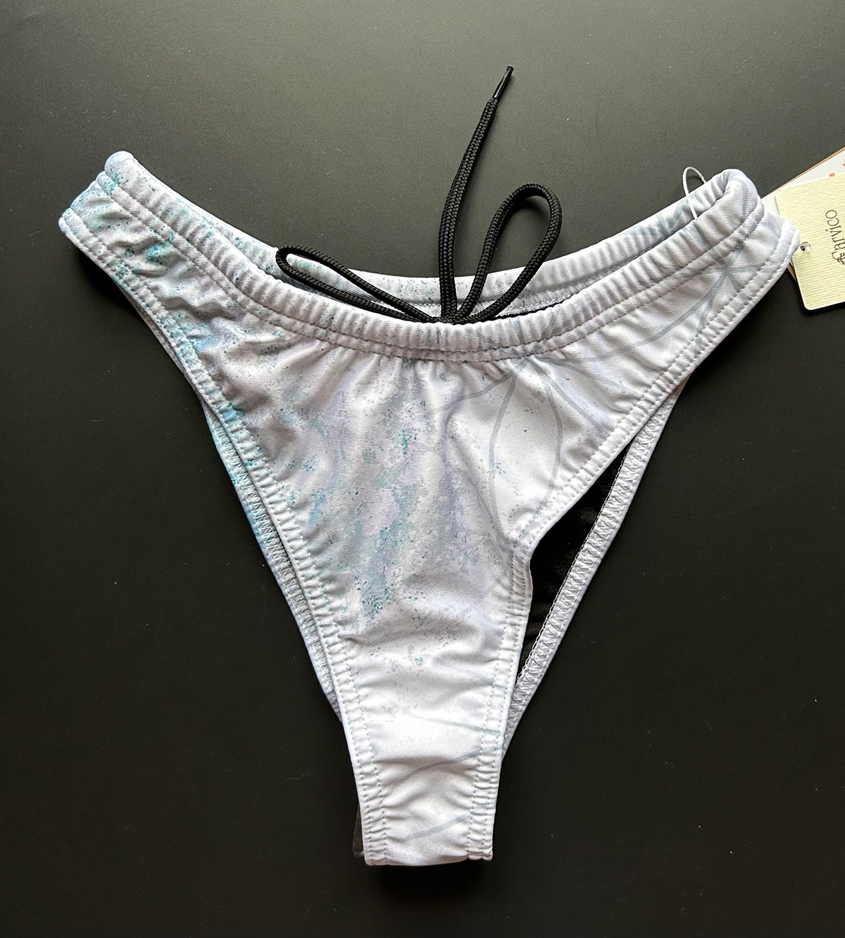 Our Flower of life – Bikini bottom shown from the front on a black surface with focus on the hand drawn pattern.