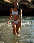 Female model wearing the Flower of life – Bikini top at the beach, walking confidently towards the camera.
