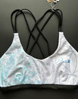 Flower of life – Bikini top shown from the front lying on a black surface, focussing on the light blue patterns and thin, black stripes.