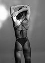 Female model wearing the Hailey One-Piece Swimsuit in color midnight in a black and white shot, shown from the back with hands on her head, highlighting the open-back design.