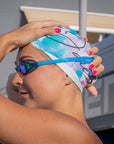 Our Model wearing the Swim Cap - Watercolor with light blue swimming googles, putting her hands on the head to put the cap in the right place for the upcoming swimming session.