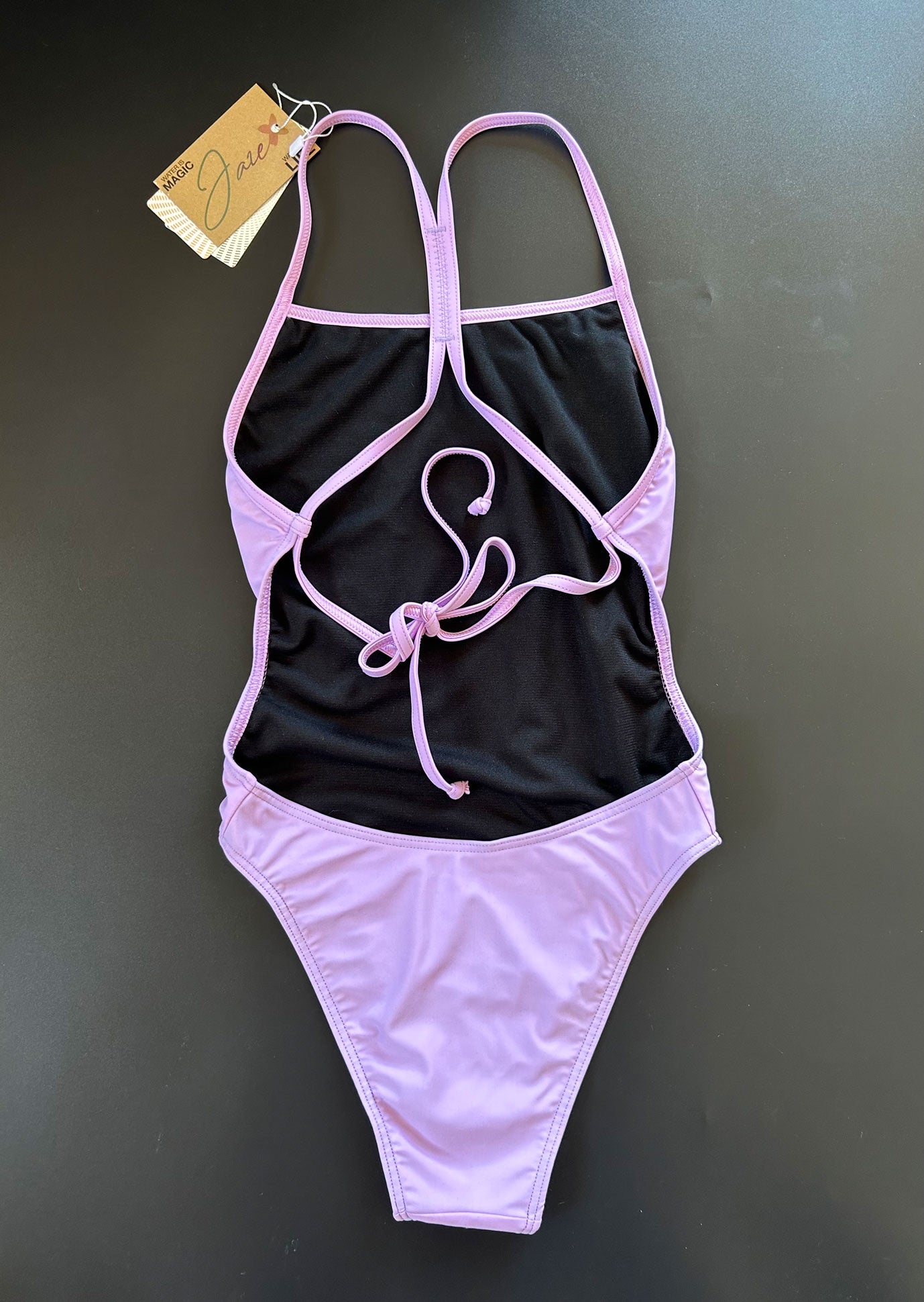 Our Lavender One-Piece-Swimsuit lying on a black surface shown from the back, showing the open back and adjustable straps.
