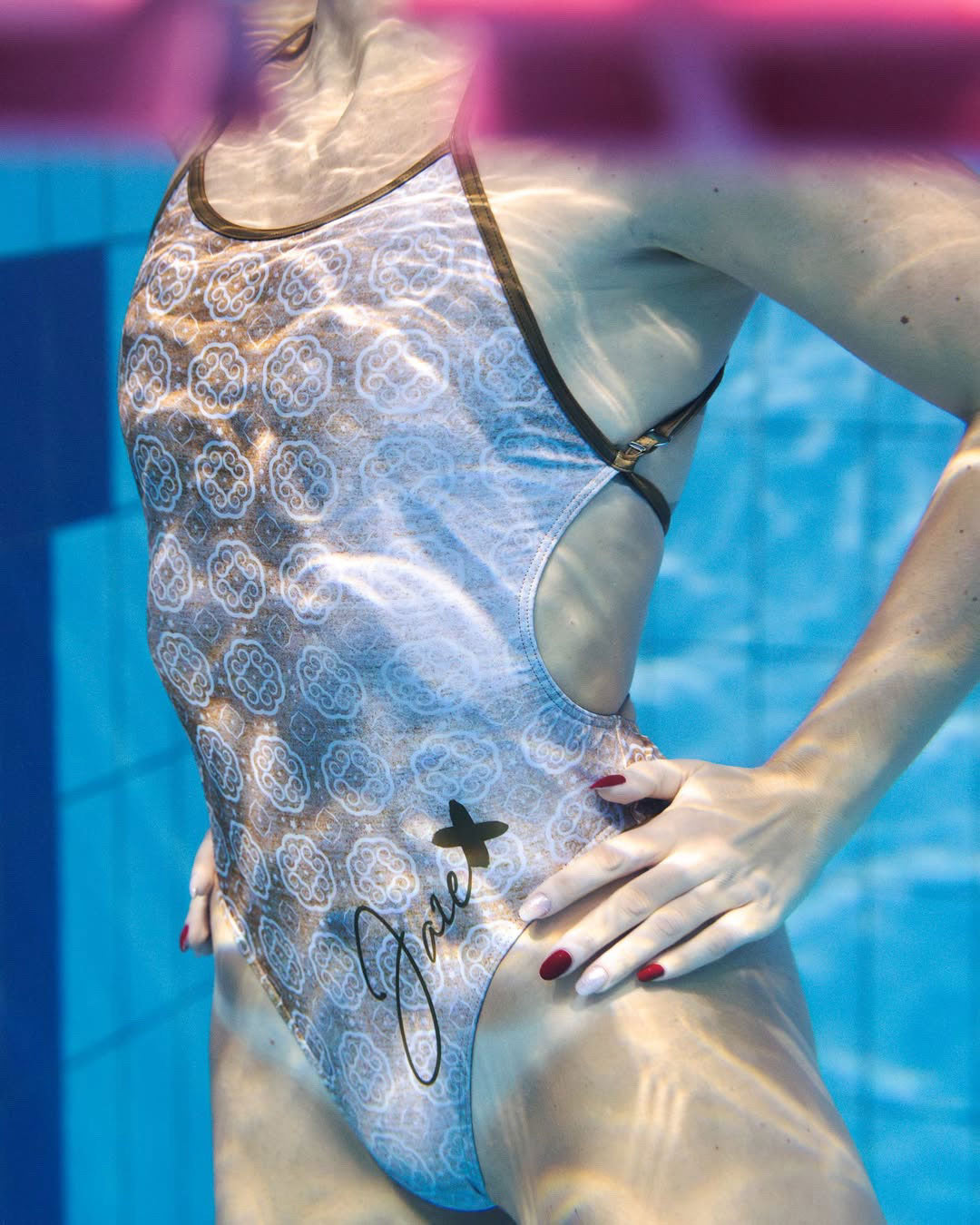 Lana one piece swimsuit shown from the side with our model in the pool with water reflections on it.