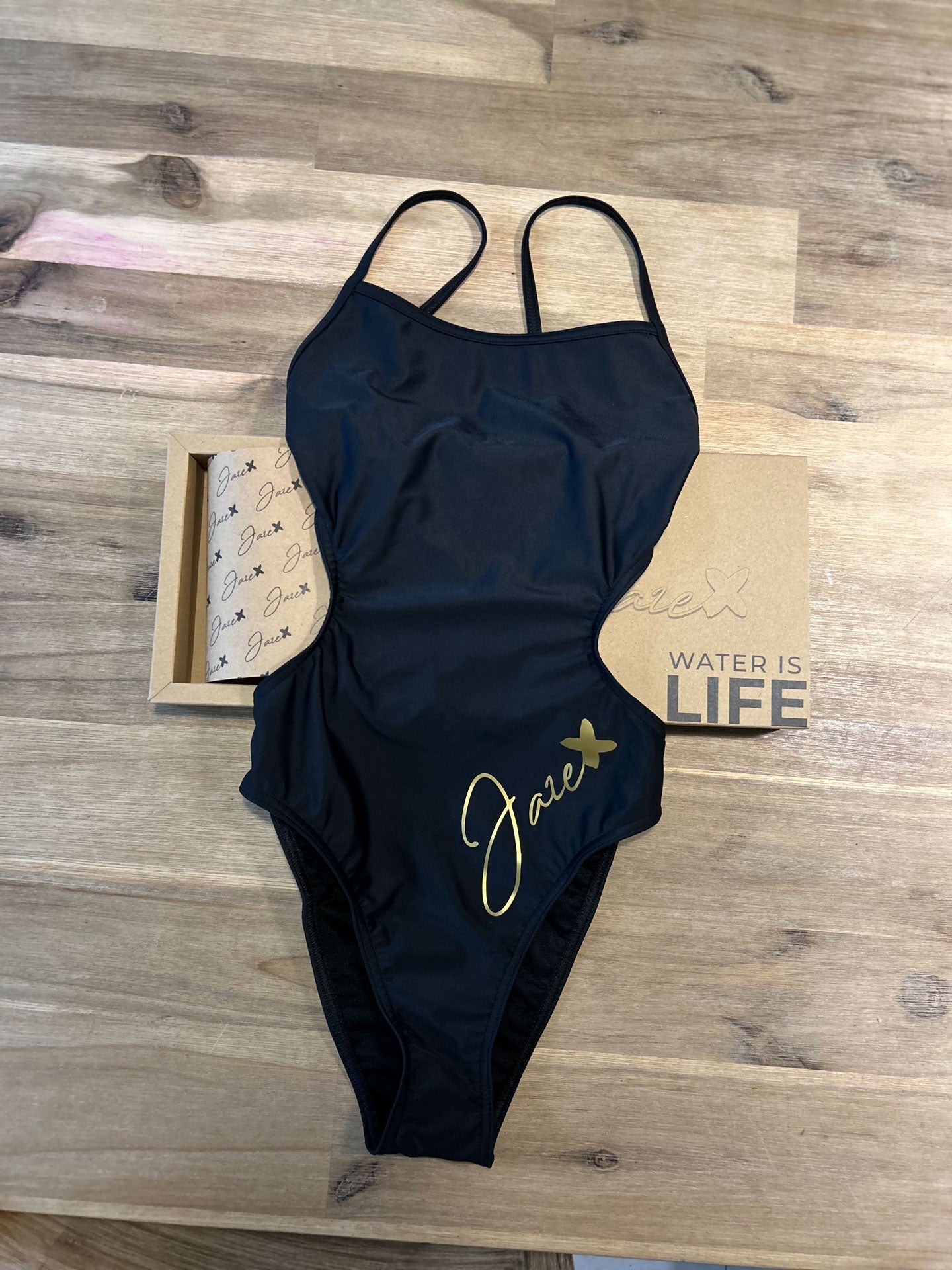 The MAYA - One-Piece Swimsuit lying on a wooden floor and shown from the front.