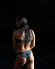 Our female Model shown from the back with our Midnight – Bikini bottom, that is dark gray in front of a black background.