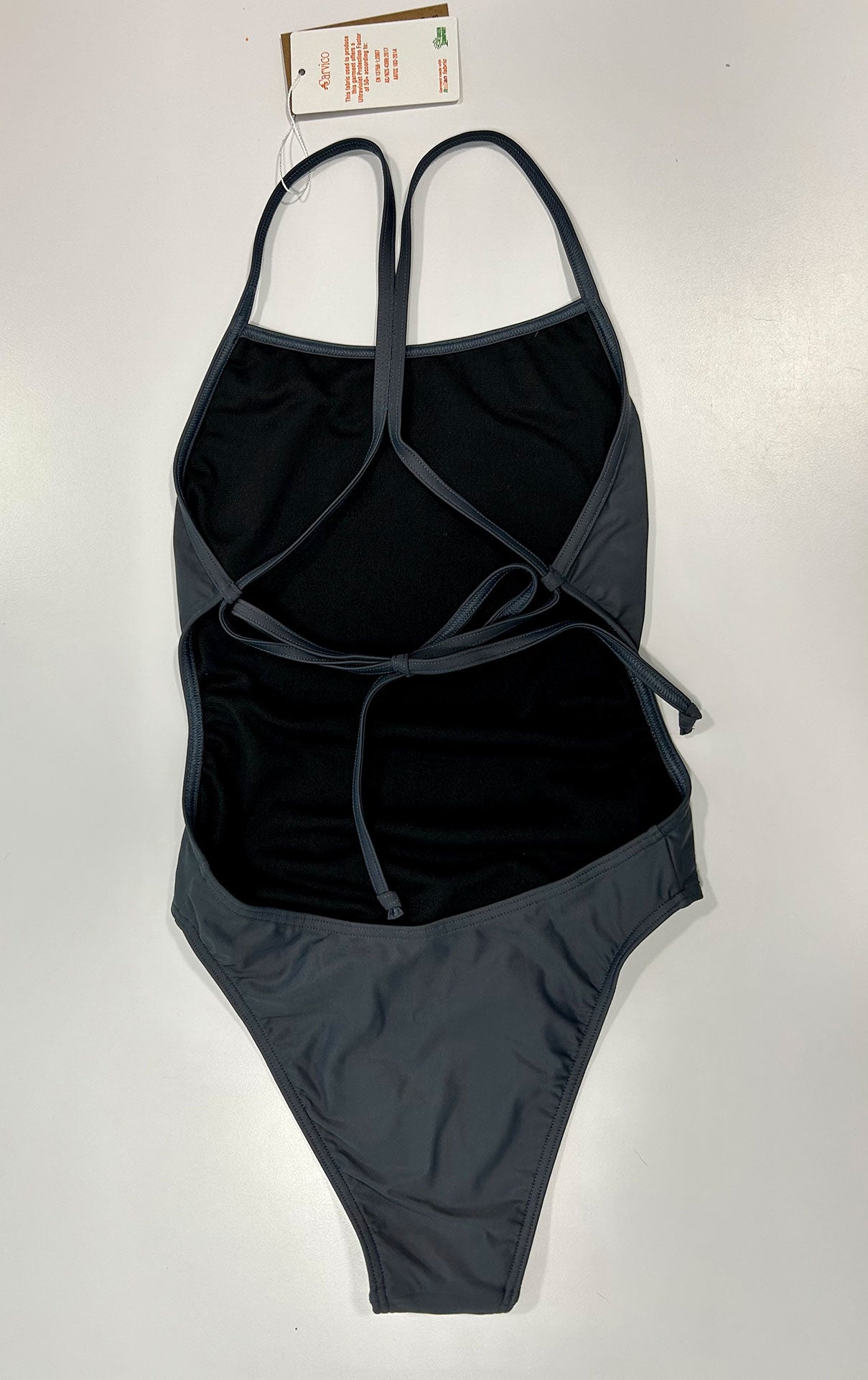 Our midnight – one piece swimsuit shown from the back, lying on an white table, where the gray color and the thin straps can be seen in more detail.