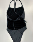 Our midnight – one piece swimsuit shown from the back, lying on an white table, where the gray color and the thin straps can be seen in more detail.