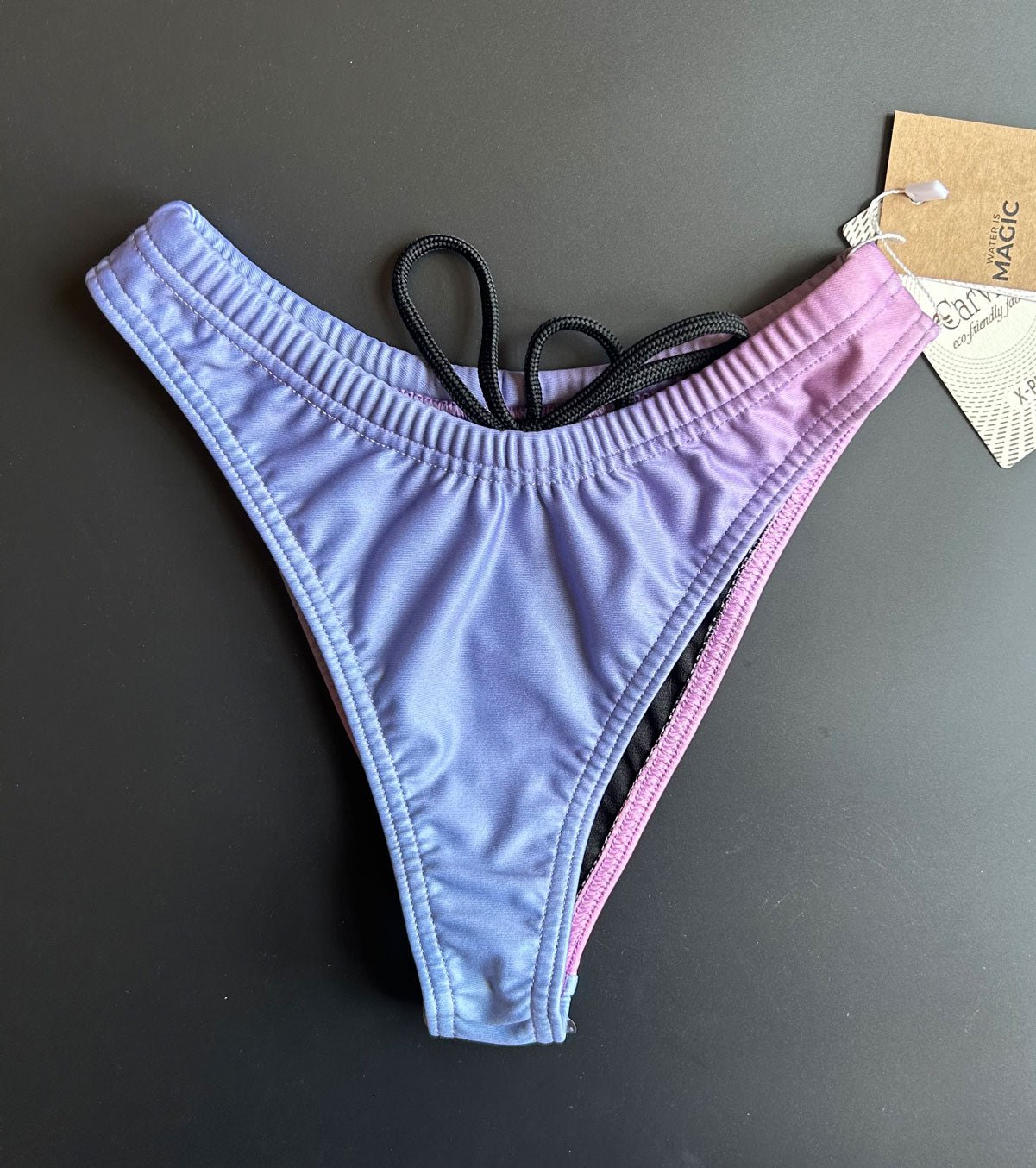 The RAINBOW – Bikini bottom lying on a black surface shown from the front comes with a high leg cut.