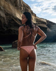 Back view of a female model in the Sunrise Swim Onesie, touching her hips and looking back at the camera, showcasing the open-back design and secure fit.