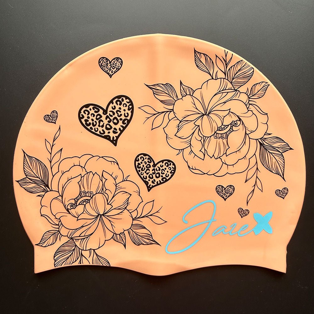The BLOOM – swim cap has a peach base and beautiful flowers and hearts painted with fine, black lines.