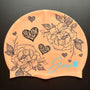 The BLOOM – swim cap has a peach base and beautiful flowers and hearts painted with fine, black lines.