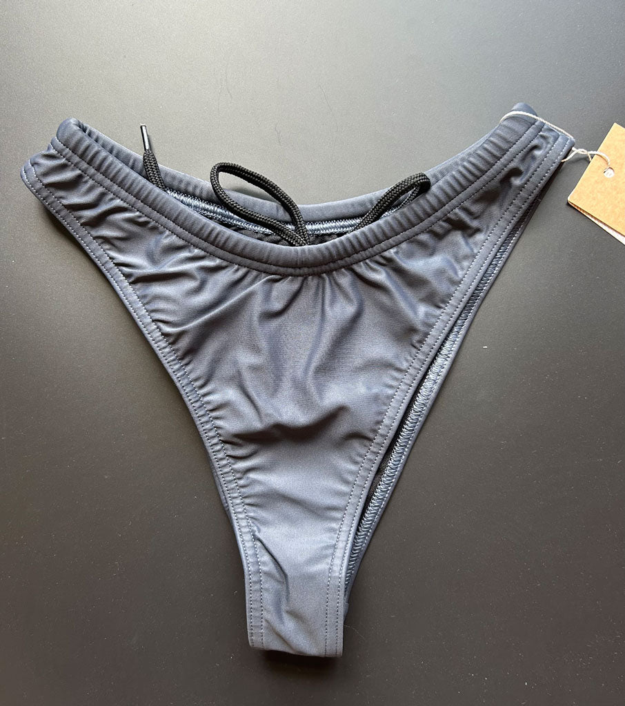 Our Midnight Bikini Bottom shown from the front, which comes in dark gray with a drawstring inside, lying on a black background for more details.