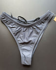 Our Midnight Bikini Bottom shown from the front, which comes in dark gray with a drawstring inside, lying on a black background for more details.