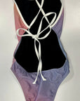 Our RAINBOW - One-Piece Swimsuit lying on a white table, where the colors and the white, thin straps can be seen in more detail. The straps in the back are tied into a stitch.