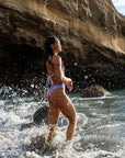 Our female Model standing on the beach and shown from the side, wearing the RAINBOW - One-Piece Swimsuit, a colorful Swimsuit turning from rose on top to violet at the bottom.
