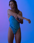 Female model in a Zebra Blue one-piece swimsuit stretching her arm forward, emphasizing the swimsuit's comfortable fit and flexible design.