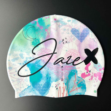 Our Jaze Swim Cap - Watercolor is a colorful Cap that has a white base with lot of symbols like hearts, moon, flowers and a beautiful splash of colours, all fluently united. The Jaze-Logo is printed on the side of the cap.