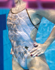 Lana one piece swimsuit shown from the side with our model in the pool with water reflections on it.