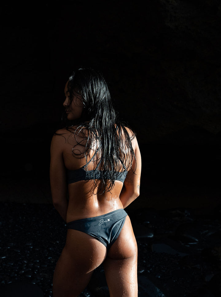 Our Model shown from the back with our Midnight – Bikini bottom, that is dark gray with a high leg cut and showing a bit more from your butt ckeeks than regular buttoms in a very athletic way.