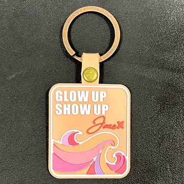 Key chain "Glow up Show up" in orange with olourful waves in orange, pink and red with jaze logo.